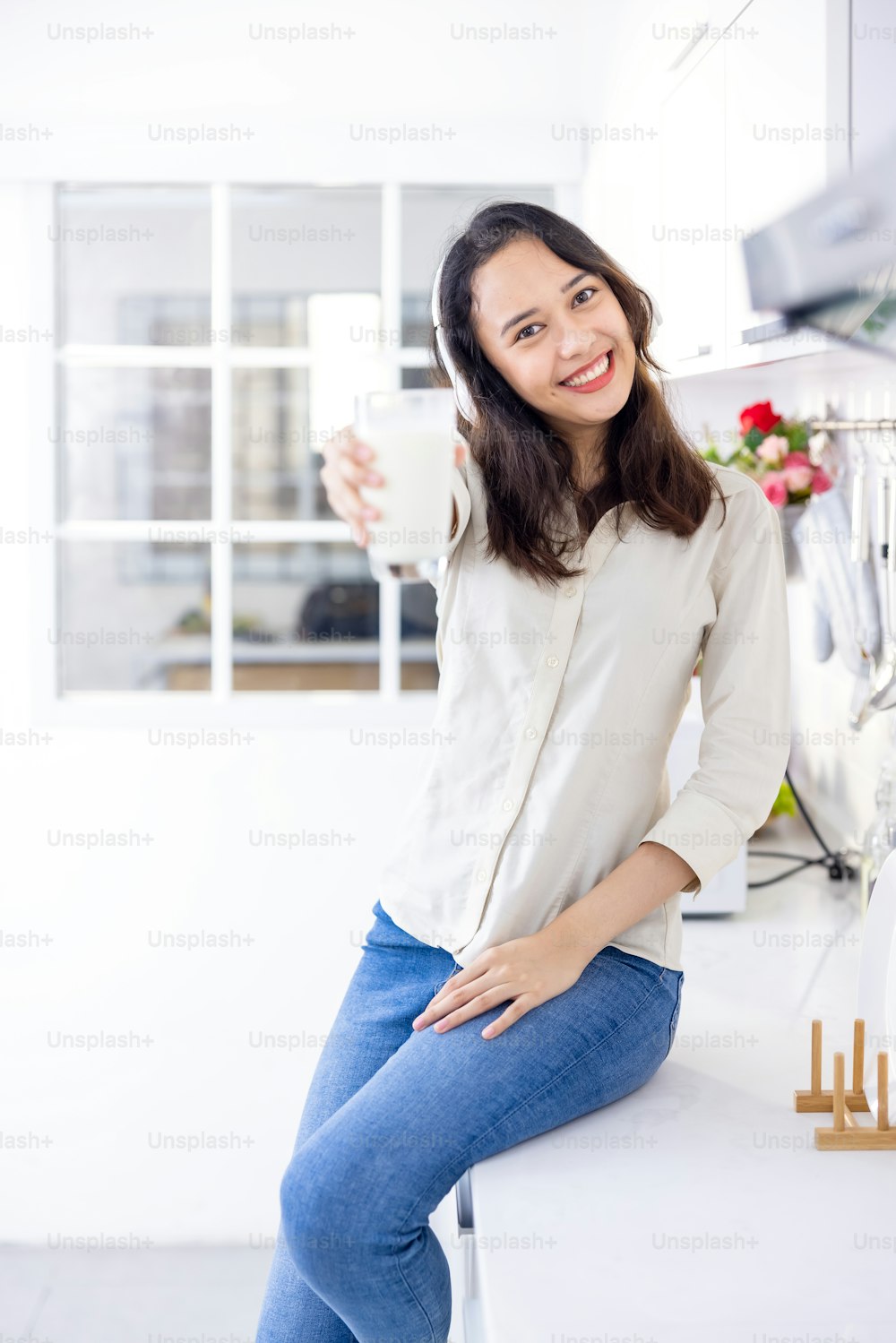 Beautiful woman drinking milk while listening to music in light modern kitchen. she is fun and smiling before breakfast.