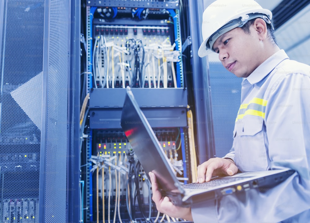 A man with a laptop sits in the server room of the data center. The system administrator works near the racks with the servers.