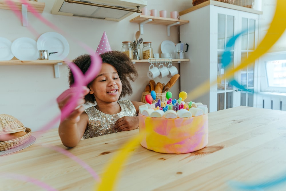 Fille heureuse regardant le gâteau d’anniversaire avec des bougies s’amusant pendant la fête d’anniversaire dans la cuisine. Mise au point sélective sur le visage de la fille.