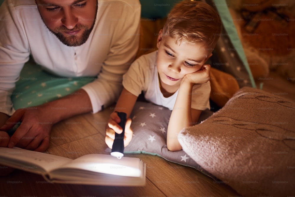 本を読んだり、懐中電灯を使ったり。お父さんと若い子がテントの近くの屋内で一緒に過ごしています。