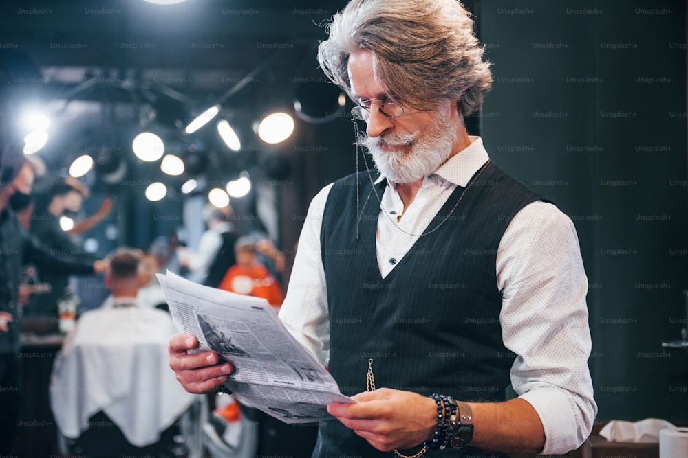 Zeitung lesen. Stilvoller moderner älterer Mann mit grauen Haaren und Bart ist drinnen.