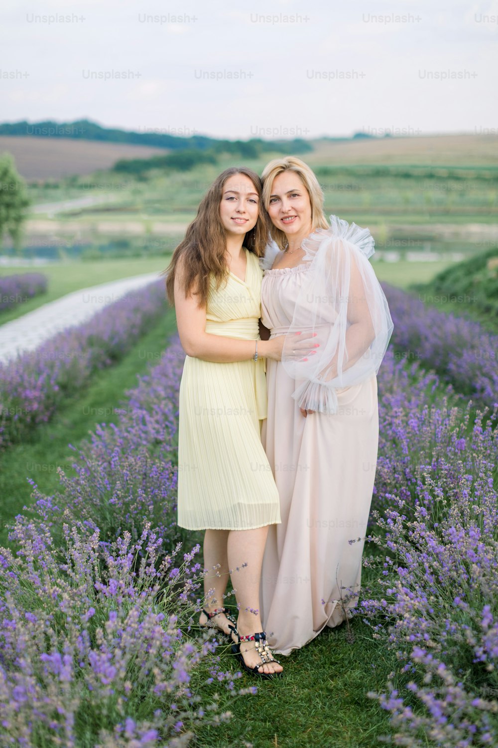 Mother and daughter in lavender field on beautiful summer day. Stunning middle aged blond lady standing at lavender field with her pretty young daughter and enjoying the walk