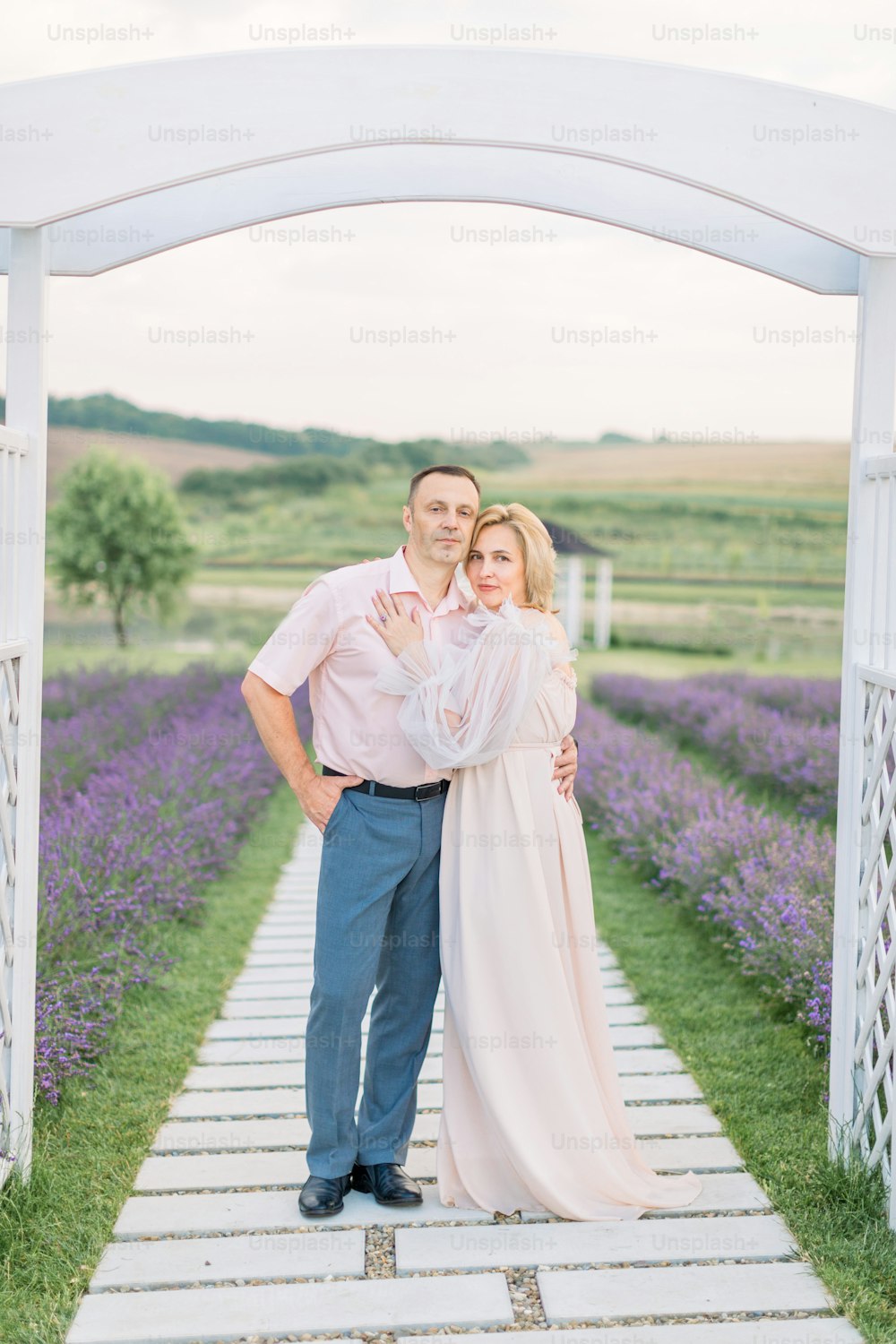 Mature couple in love standing outdoors under the wooden arch in lavender field, spending romantic date and anniversary celebration. Wedding, love and family concept