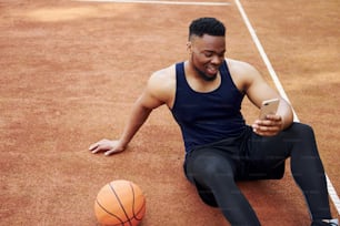 전화 사용. 아프리카 계 미국인 남자는 야외에서 코트에서 농구를합니다.