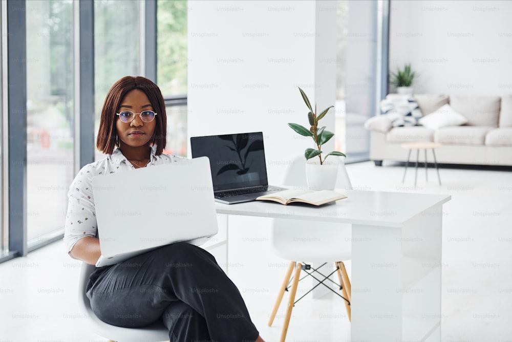 Young african american woman in formal clothes is in the office with laptop.