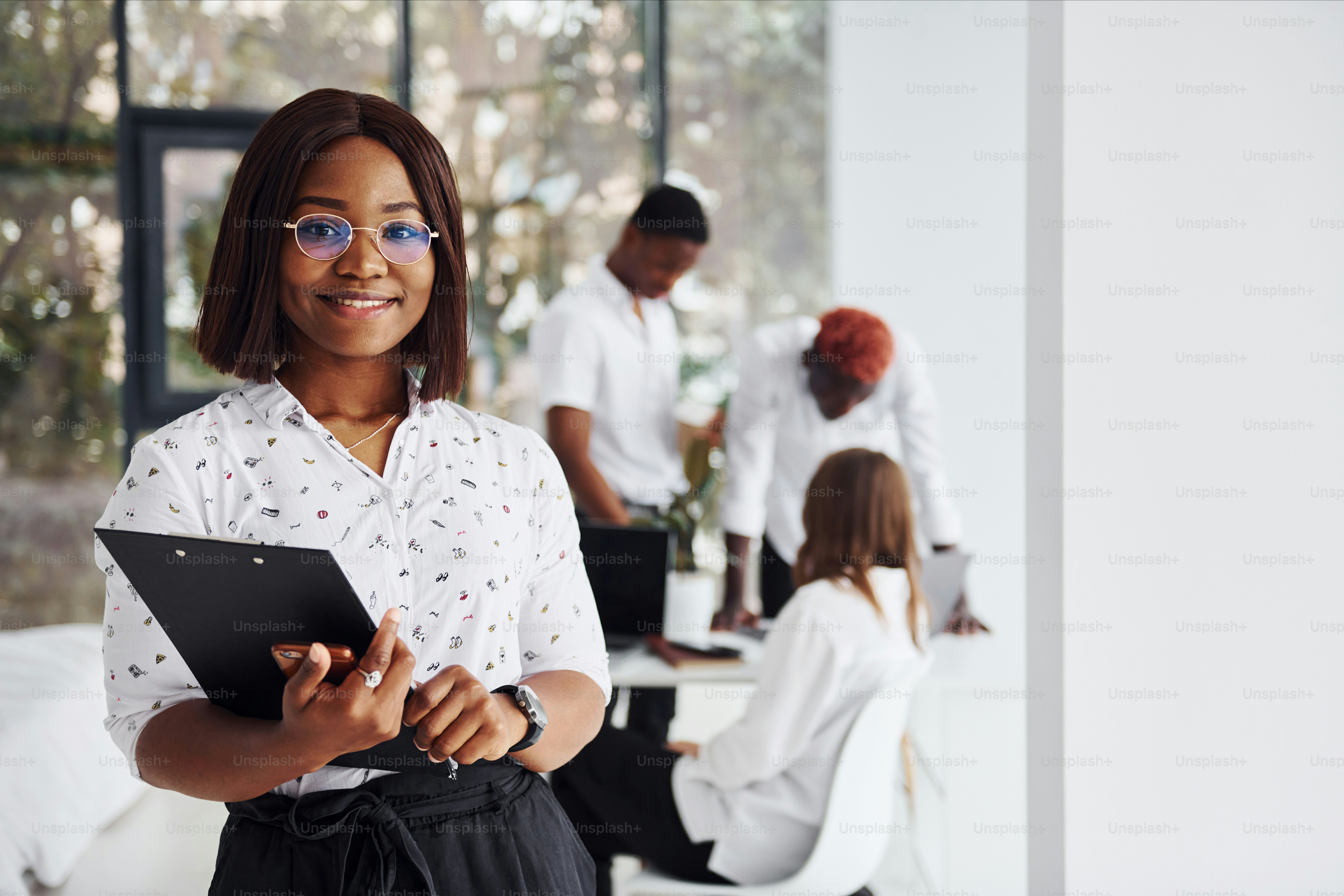 Schöne Frau in Brille vor ihren Kollegen. Gruppe von afroamerikanischen Geschäftsleuten, die zusammen im Büro arbeiten.