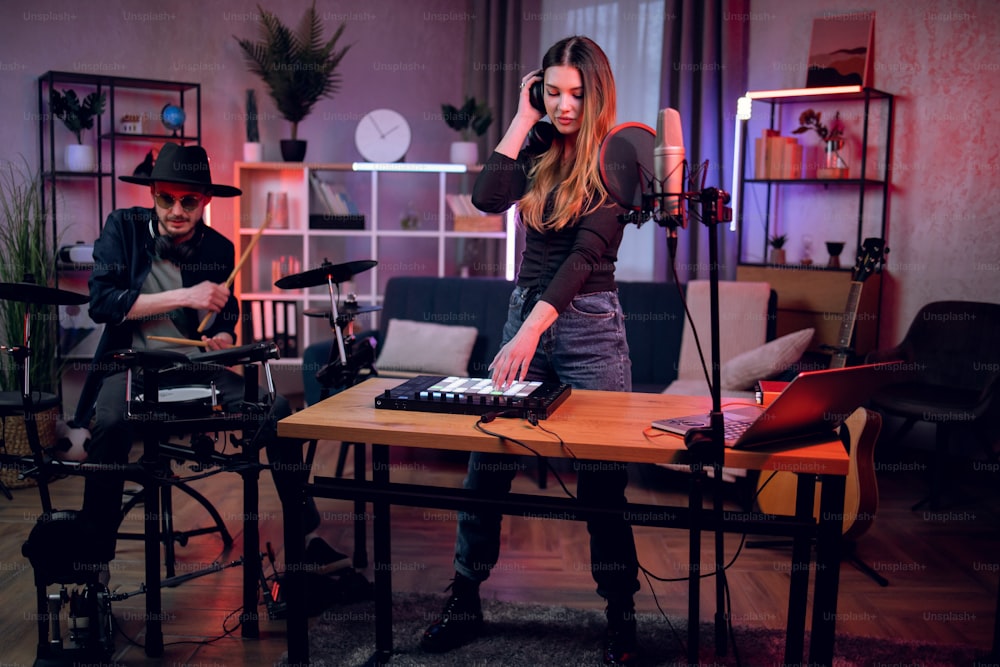 Uomo e donna caucasici che utilizzano un laptop moderno per lo streaming di video dal vivo mentre suonano su strumenti elettronici in home studio. Concetto di persone, musica e tecnologia.