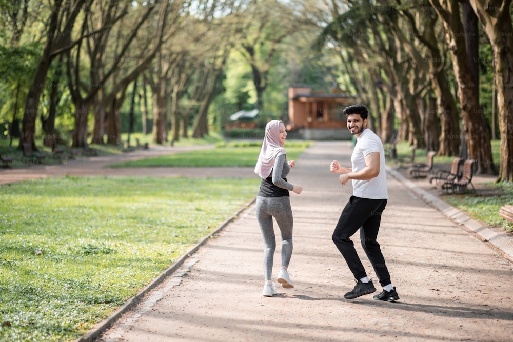 Pareja árabe feliz en ropa deportiva trotando en el parque verde durante la mañana. Hombre y mujer jóvenes que disfrutan del tiempo que pasan juntos. Entrenamiento común al aire libre.