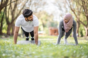 ヒジャーブとアクティブウェアを身に着けた若いイスラム教徒の男女が、緑の夏の公園で板張りの姿勢で立っている。新鮮な空気の中でのスポーツとフィットネス。