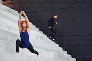 Dos amigas con cuerpos deportivos haciendo ejercicios en las escaleras al aire libre.