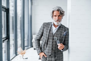 De pé na sala. Homem moderno elegante sênior com cabelos grisalhos e barba dentro de casa.