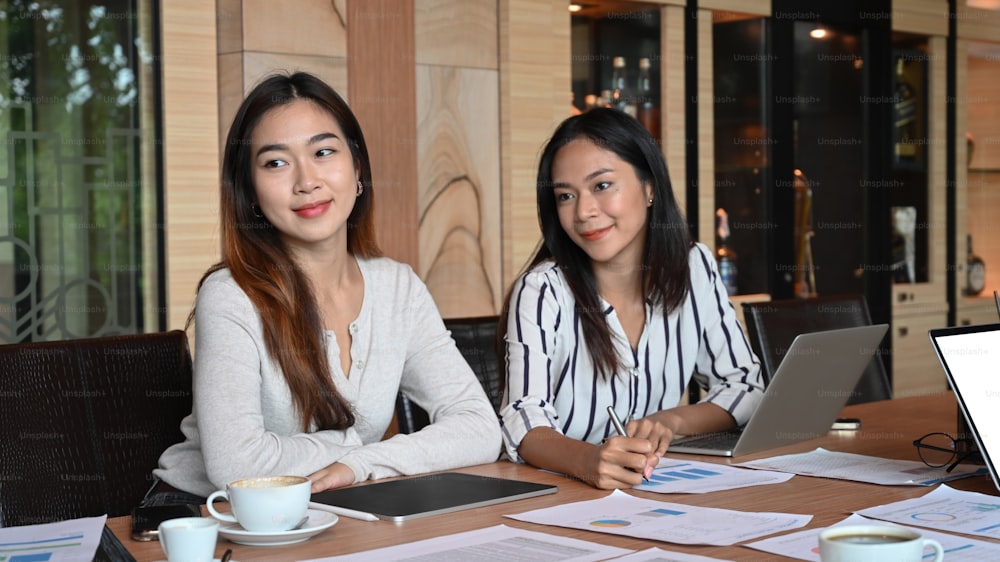 Two smiling businesswomen sitting at boardroom table during an office meeting.