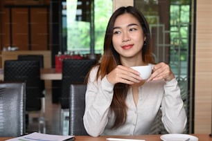 사무실에 앉아 커피를 마시는 행복한 젊은 여성.