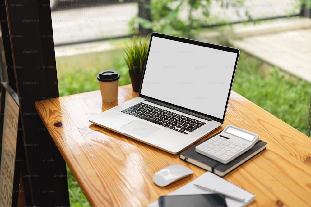 Ordinateur portable maquette d’image écran blanc avec calculatrice, tasse à café et trucs sur une table en bois dans un espace de co-working café