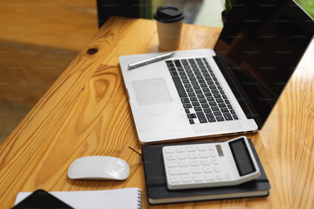 Laptop com maquete de tela vazia preta, calculadora e coisas na mesa de madeira