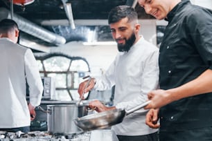 People in white uniform cooking food at kitchen together. Busy day at work.