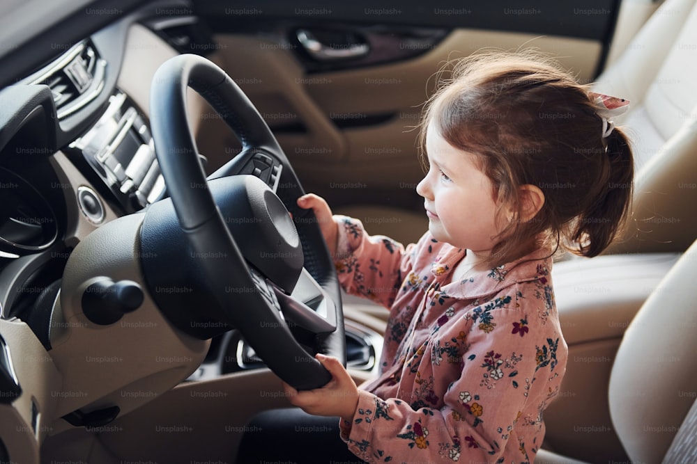 Süßes kleines Mädchen, das auf dem Fahrersitz in einem modernen Auto sitzt.