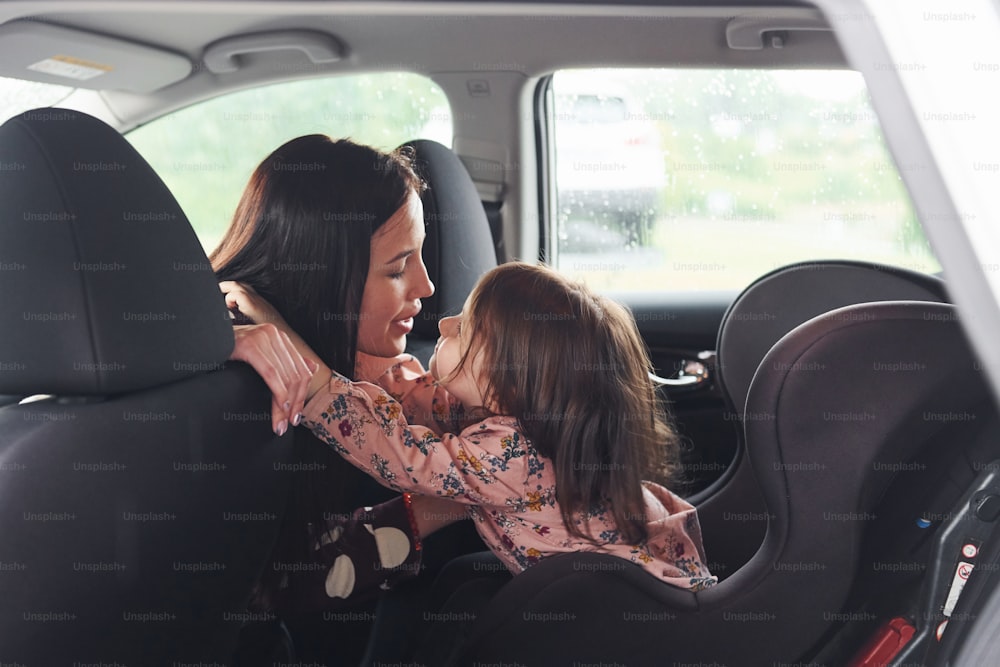 Embracing each other. Mother with her daughter inside of modern automobile together.