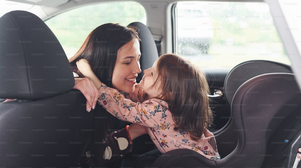 S’embrasser les uns les autres. Mère avec sa fille à l’intérieur d’une voiture moderne ensemble.