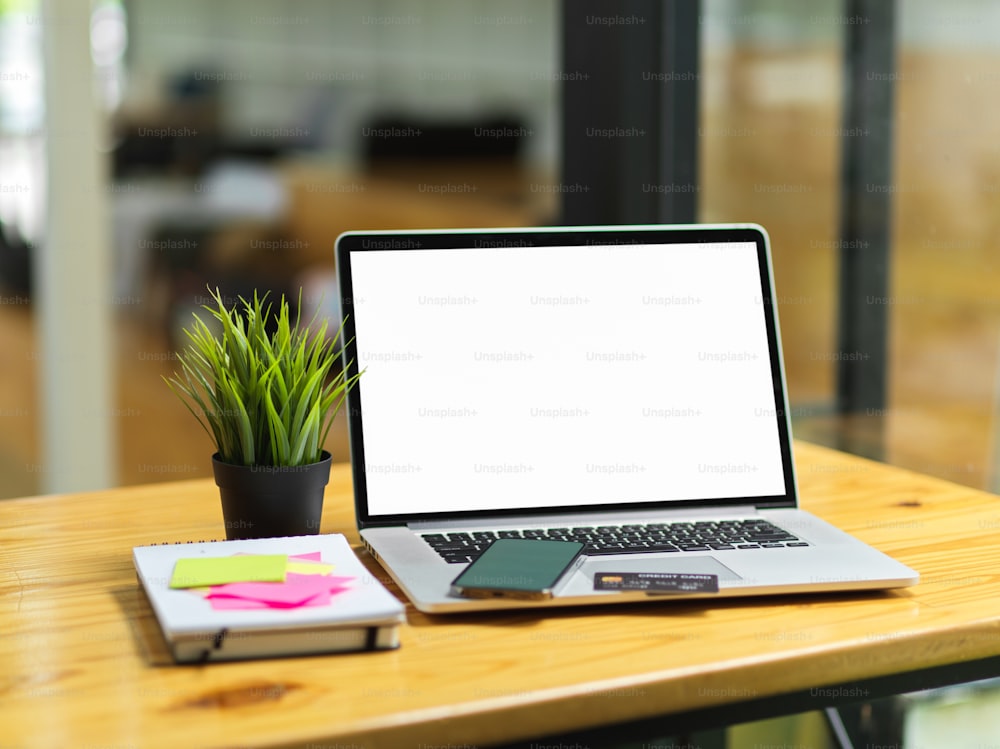 Portable laptop with blank empty screen monitor, smartphone, credit card, sticky notes and stuff on wooden table with blurred in the background