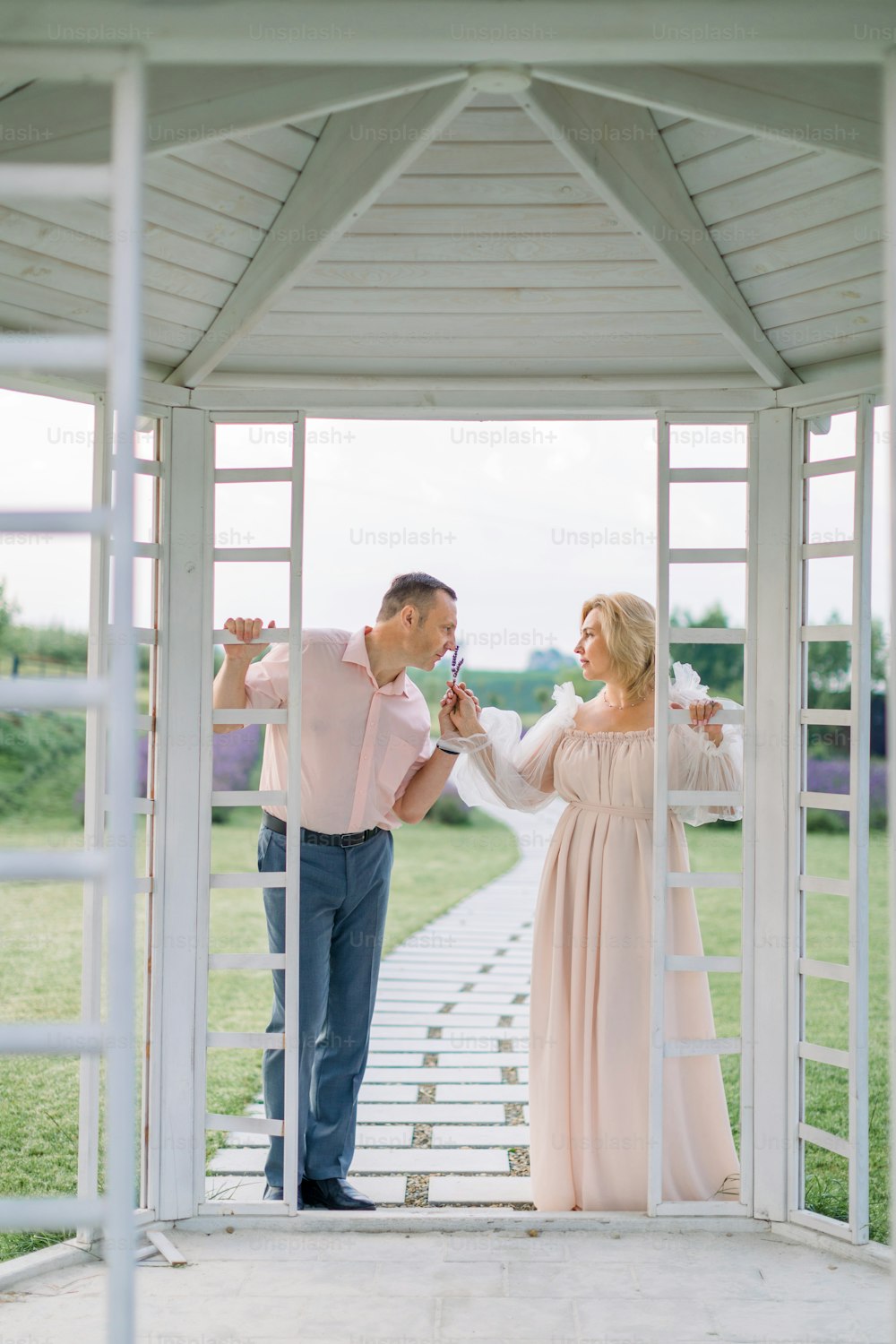 Happy pleasant mature couple in love, standing together outdoors in wooden gazebo and enjoying the scent of lavender. Romantic date, wedding anniversary celebration
