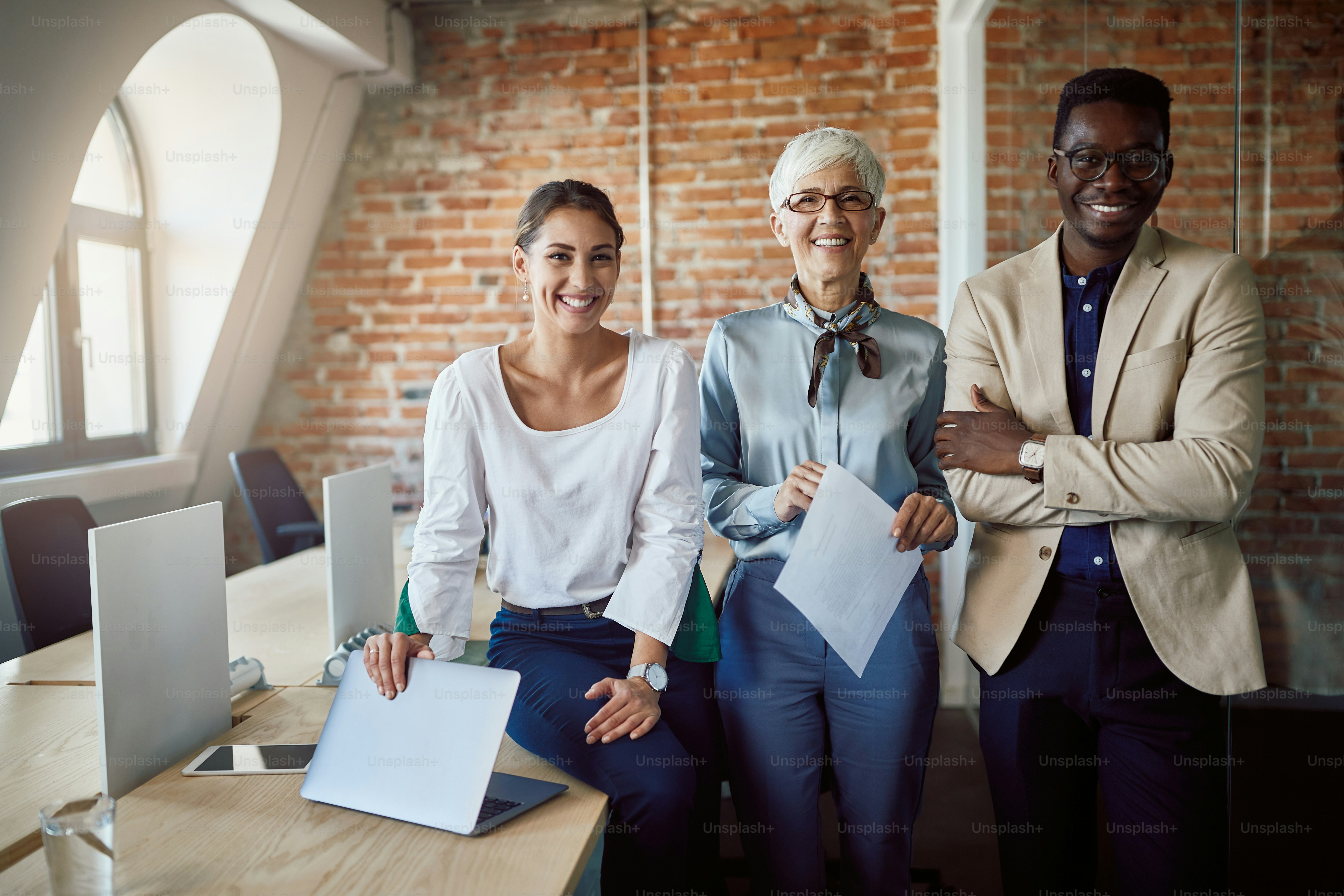 Group of happy multi-ethnic business colleagues working together at corporate office and looking at camera.