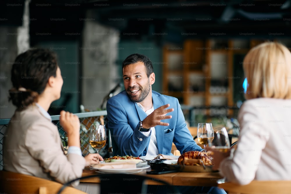 Group of business people eating lunch and talking in a restaurant. Focus is on businessman.