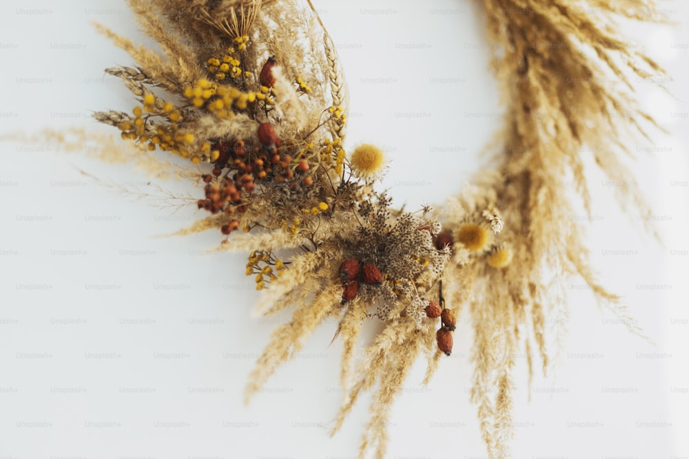 Stylish autumn rustic wreath isolated on white, details close up. Creative boho wreath with dried pampas grass, wildflowers, wheat,  berries on white wall. Hello Fall. Happy Thanksgiving