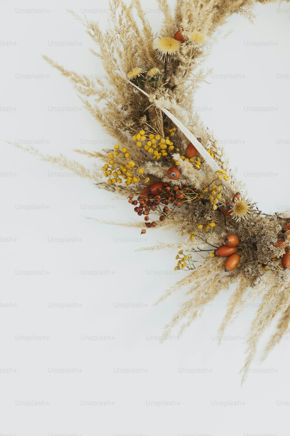 Creative boho wreath with dried pampas grass, tansy wildflowers, wheat, dog-rose berries on white wall. Hello Fall. Stylish autumn rustic wreath isolated on white, close up. Happy Thanksgiving