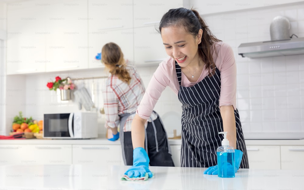 Portrait of cheerful young housewife holding cleaning supplies, smiling and looking at camera in kitchen. Professional cleaning service specialist offering help with domestic duties"n
