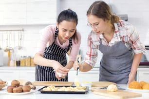 クッキーを焼く女の子、多民族の10代の女性2人がパンを焼いています。自宅のキッチンでベーカリー。若者のための週末の料理活動。ライフスタイルのコンセプト。自宅待機中のオンライン料理教室。