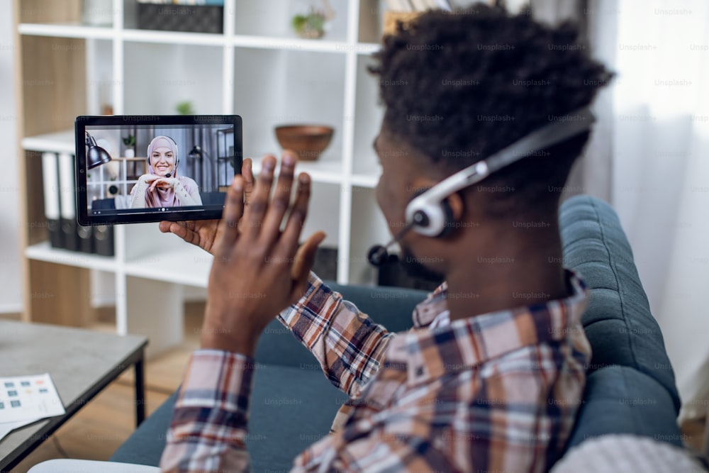 Close up of male hand holding digital tablet with muslim woman in hijab on screen. Young african man talking with girlfriend through video call during pandemic.