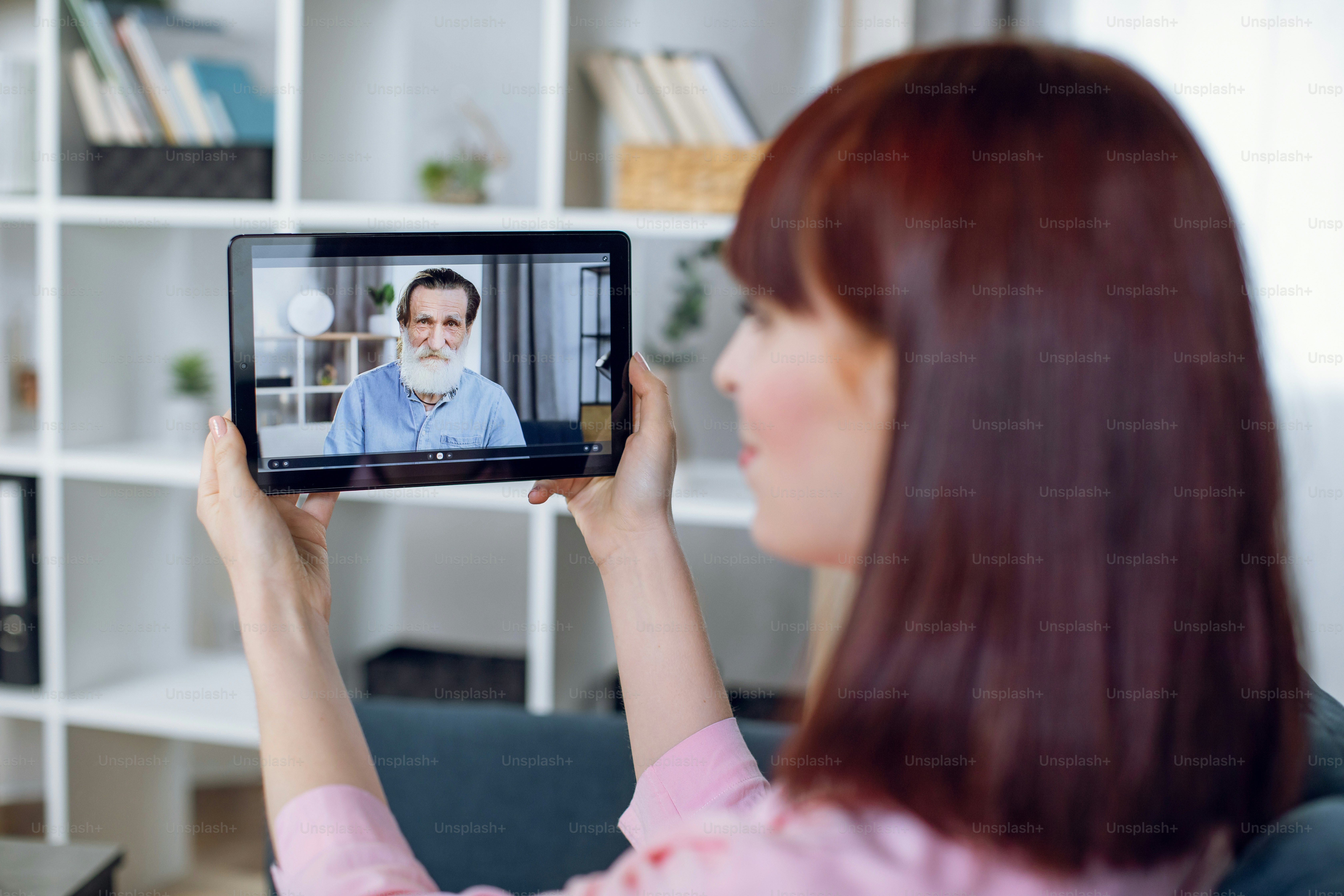 Eine Frau hält ein Tablet, das ein Videoanruf mit einem älteren Mann zeigt