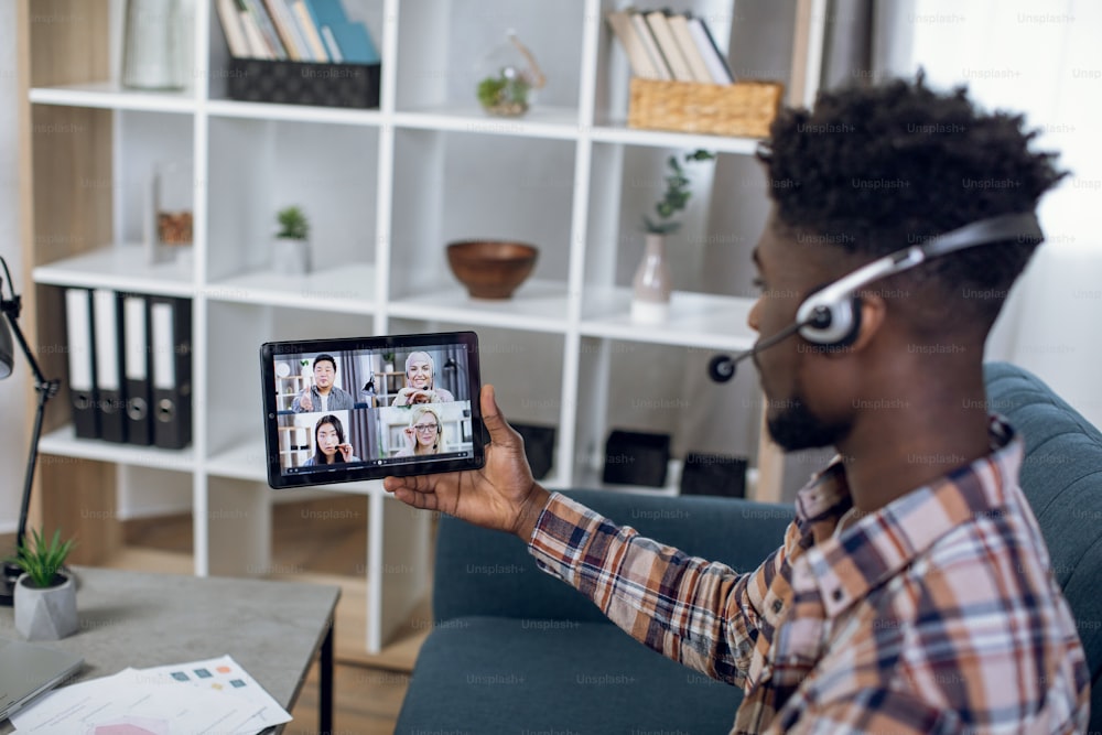 Afro american guy in headset having video conference with multiracial colleagues on digital tablet. Diverse people staying at home and cooperating on distance.