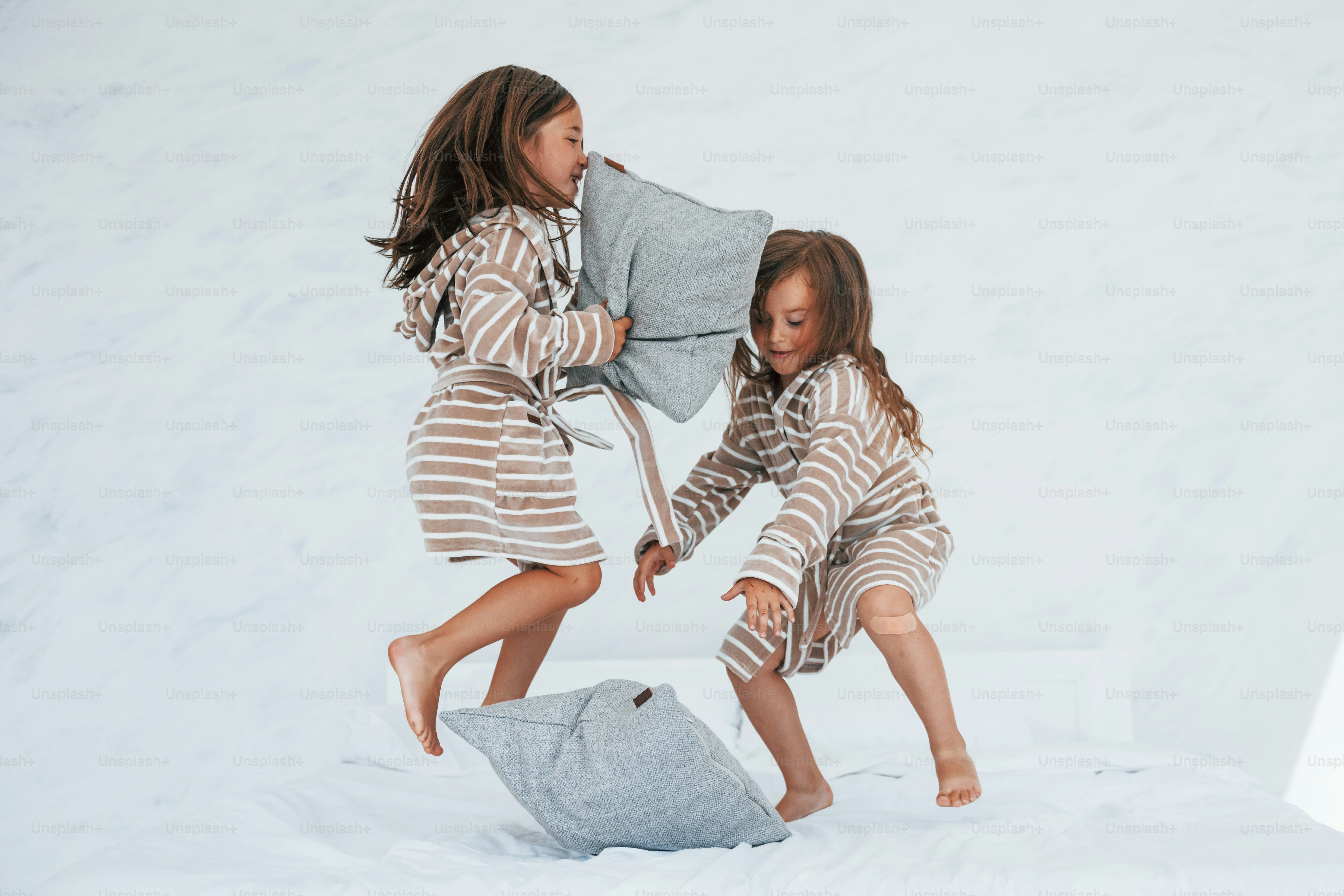 With pillows in hands. Two cute little girls indoors at home together. Children having fun.