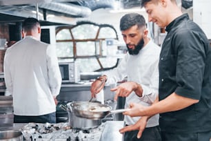 People in white uniform cooking food at kitchen together. Busy day at work.