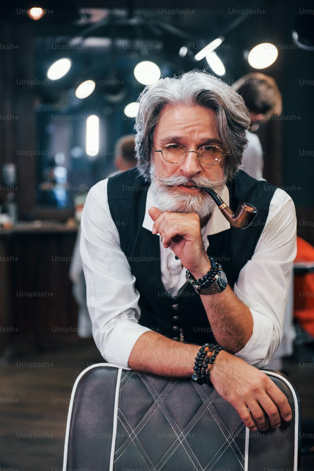 En ropa retro en barbería. Elegante hombre mayor moderno con cabello gris y barba está en el interior.