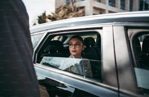 Good looking senior business man and his young woman colleague or coworker sitting on backseat in luxury car. They talking, smiling and using laptop and smart phones. Transportation in corporate business concept.