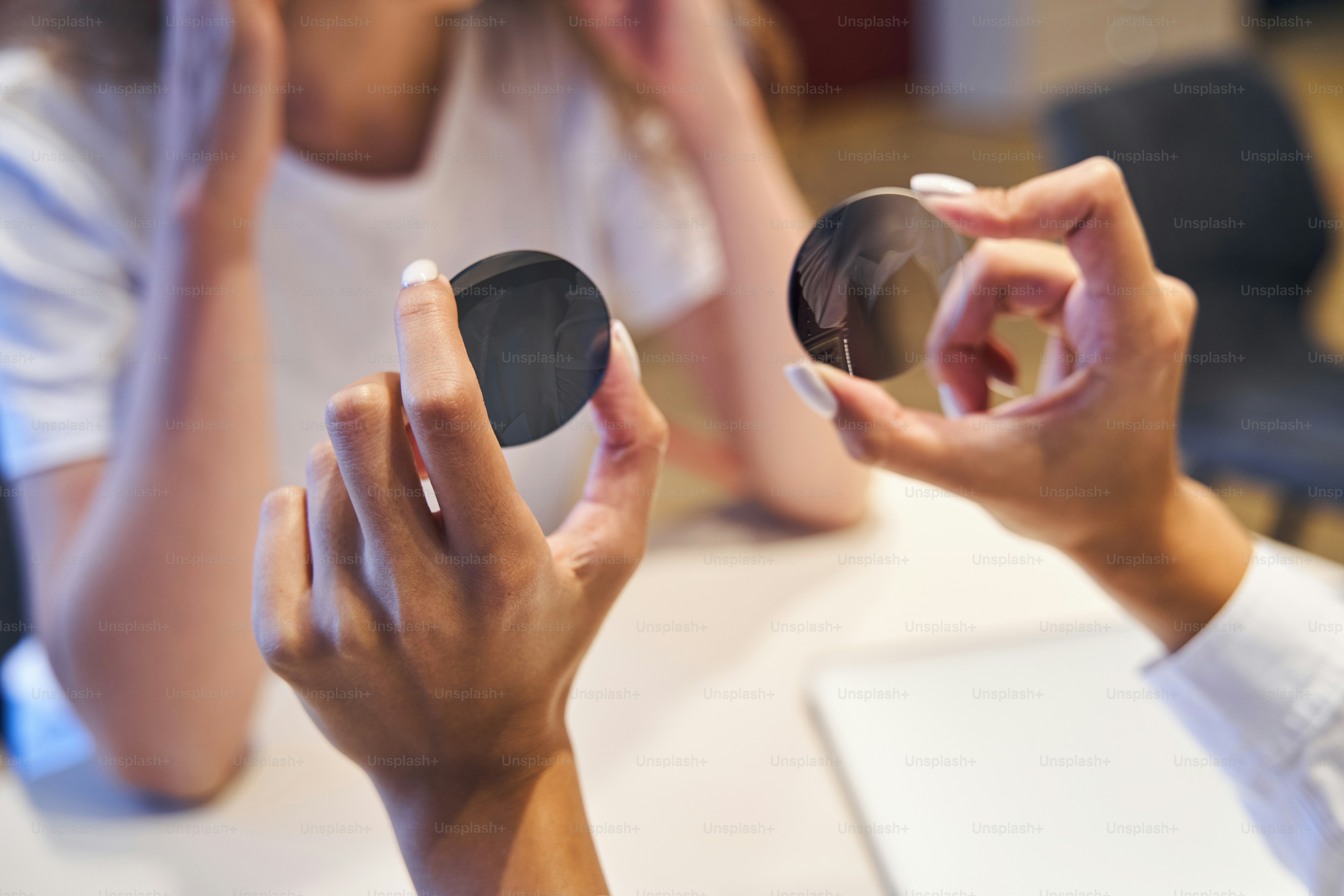 Close up of optometrist holding two round lenses while having appointment with young woman