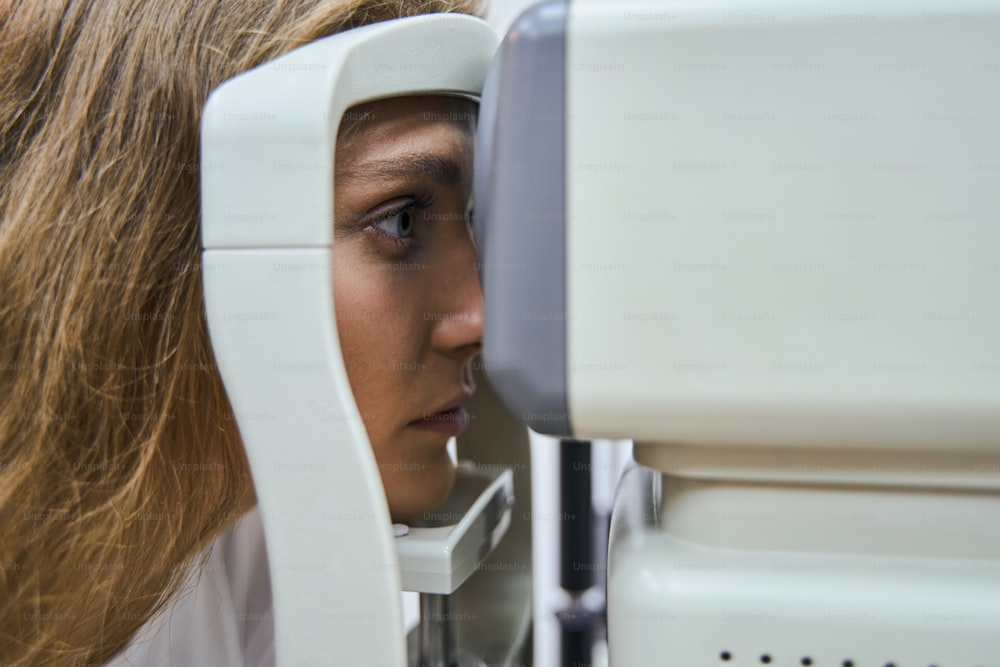 Close up of serious female patient looking through autorefractor during eyesight exam