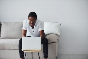 Giovane uomo afroamericano in abiti formali all'interno con laptop in mano.