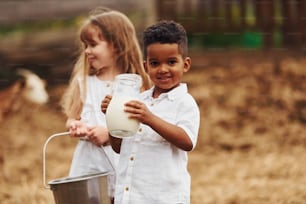 Cute little african american boy with european girl is on the farm with milk.