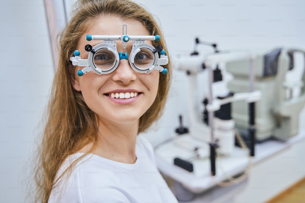 Smiling female patient using ophthalmic testing device during eye examination in clinic