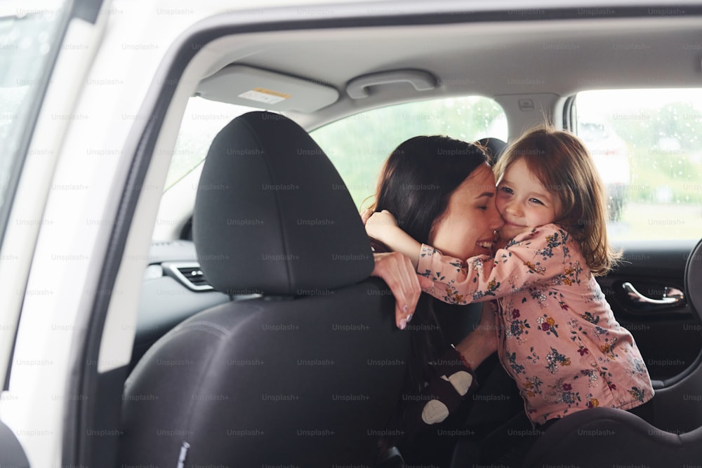 Abraçando-se. Mãe com sua filha dentro do automóvel moderno juntos.