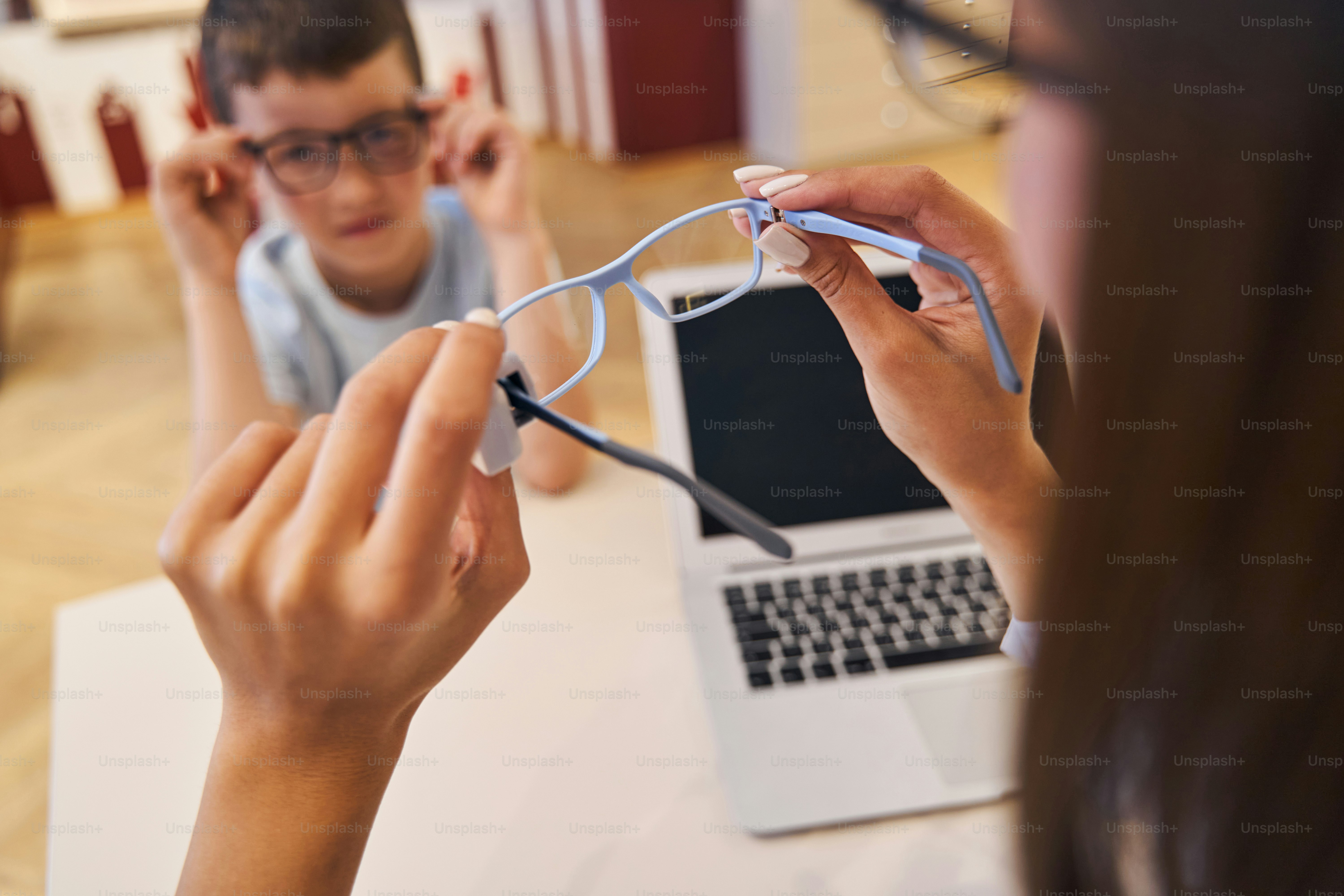 Close up of female hands holding glasses while male kid sitting at the table with modern laptop