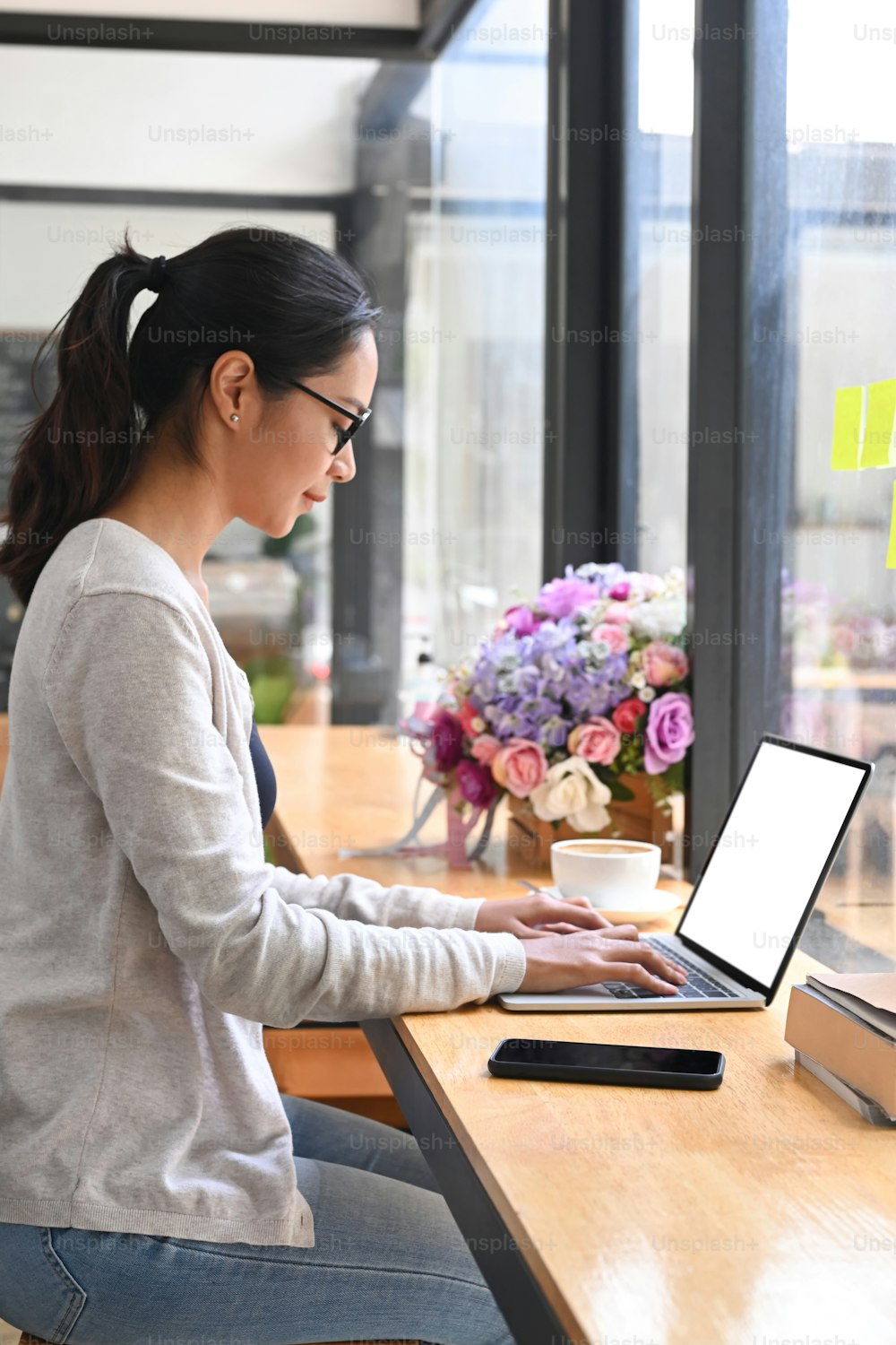 Vista lateral jovem freelancer do sexo feminino sentado no café e trabalhando on-line com laptop.