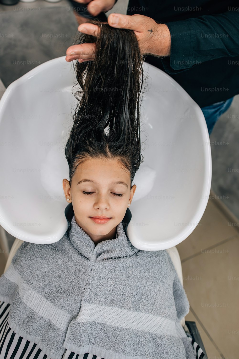 전문 미용사가 부드럽게 머리를 씻는 동안 헤어스타일 치료를 받는 어린 소녀.