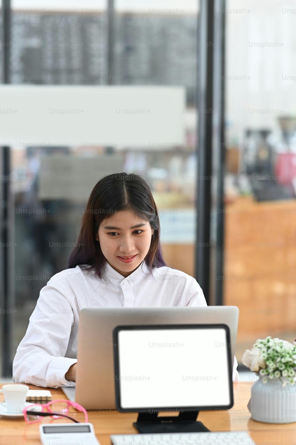 Employée souriante assise dans un bureau moderne et travaillant avec un ordinateur portable.
