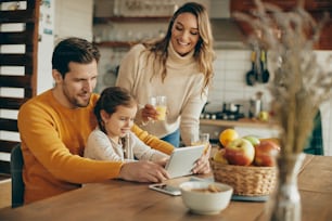 Young happy parents with daughter using touchpad while relaxing at home.