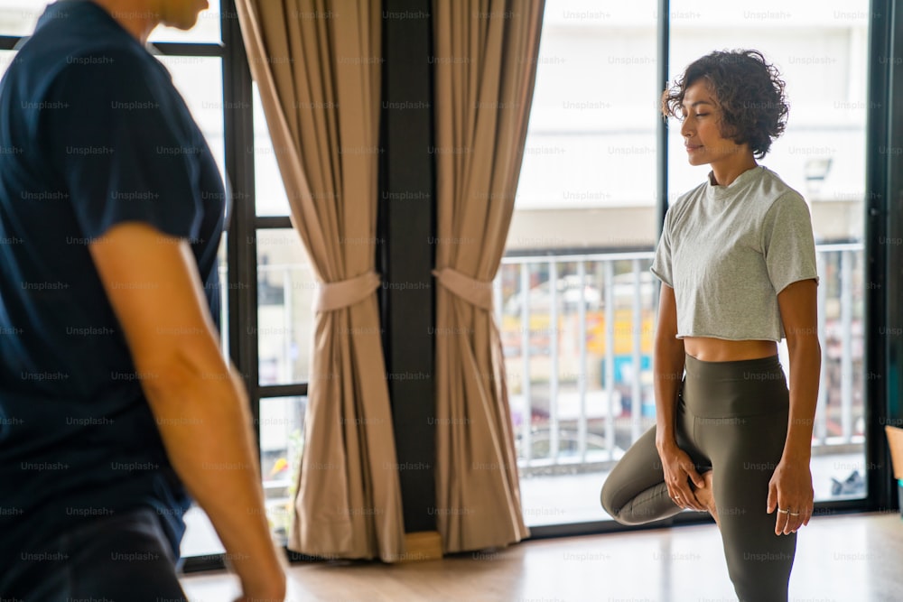 Il gruppo di donne asiatiche sane fa pratica di yoga e lezione di esercizi di fitness per lo stretching del corpo insieme all'istruttore maschio nello studio di yoga. Le amiche amano l'attività al chiuso, lo stile di vita e l'allenamento sportivo.